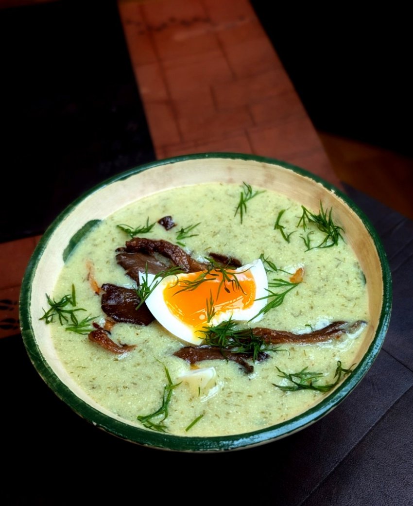 A portrait close-up of creamy Kulajda, a traditional Czech dill and mushroom soup, highlighting the rich texture and fresh herb garnish.