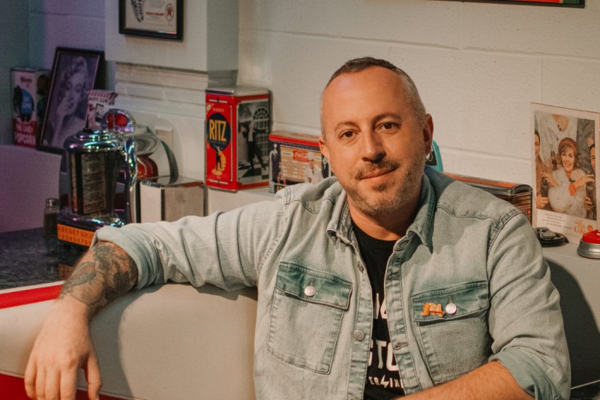 Cookbook author Dan Clapson in a denim shirt, sitting in diner booth for a portrait.