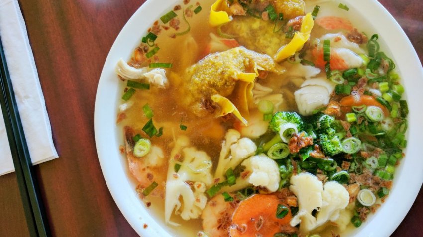 A bowl of Vietnamese-style wonton soup from Nho Saigon in Calgary with vegetables, prawn wheat noodles, fried shallots and crispy wontons.