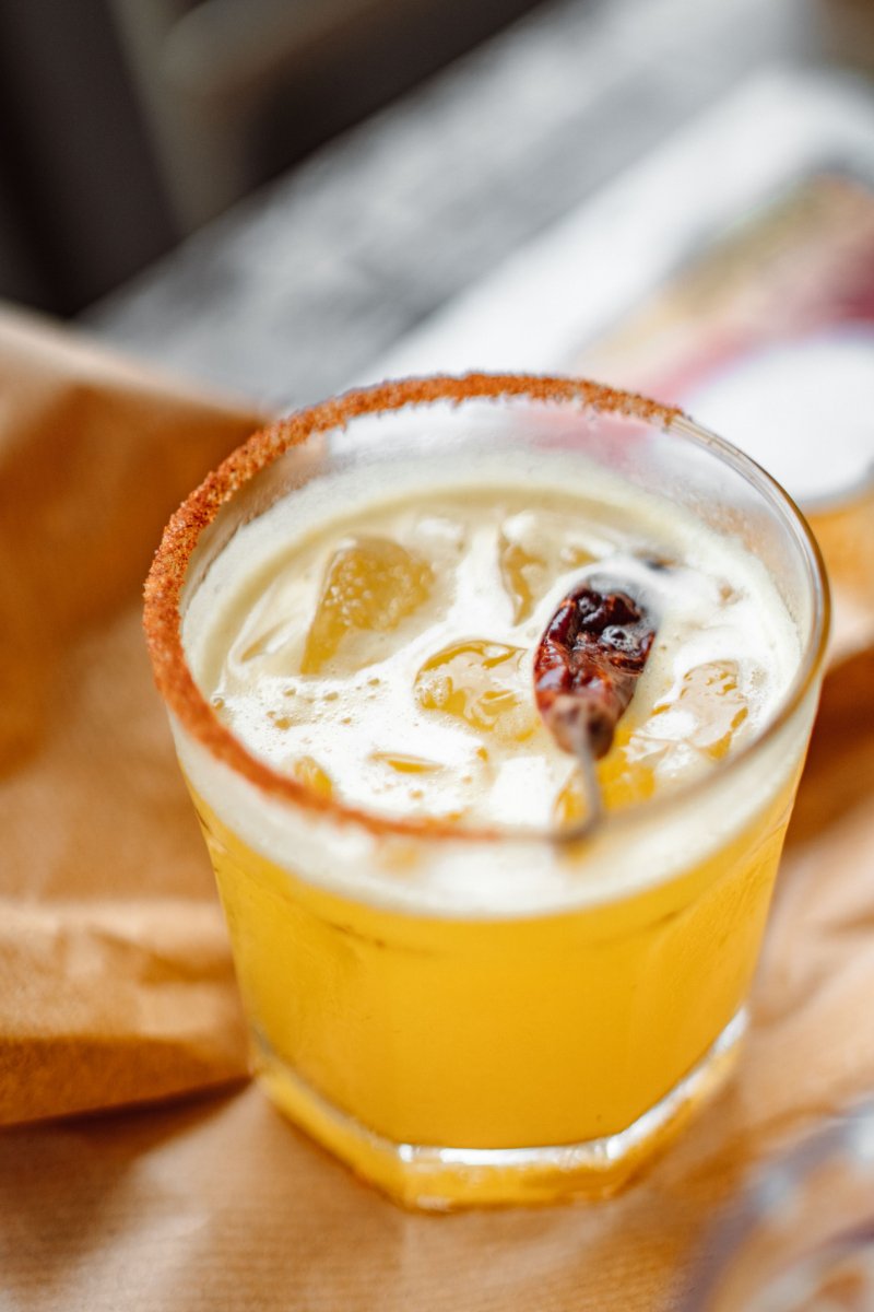 Close-up side view of the Plain Jane Gold cocktail showing its golden turmeric hue and dehydrated citrus garnish.