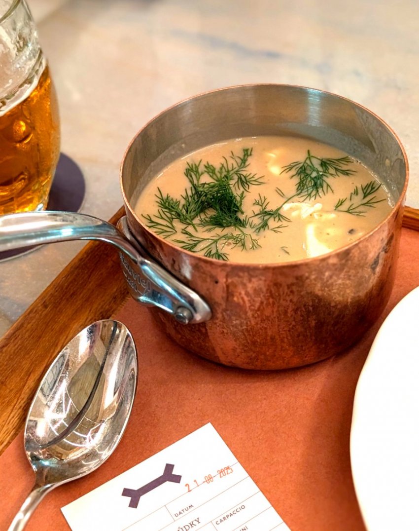 A traditional serving of Kulajda soup presented in a small copper pot on a tray at Kantýna, a famous bistro in Prague