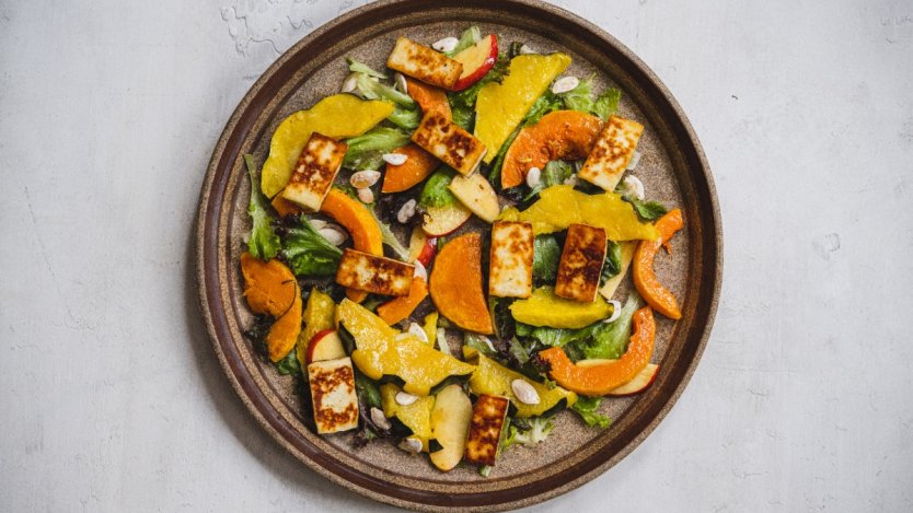 A cermaic brown plate with roast squash, greens, apple slices and grilled halloumi. A recipe from Dan Clapson's cookbook Prairie.